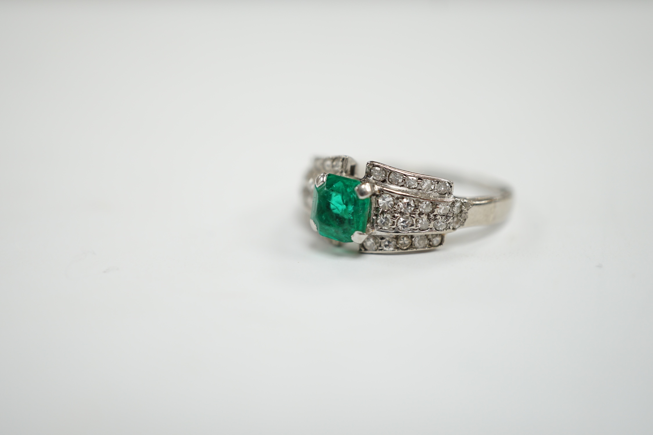 A white metal and octagonal cut emerald set dress ring, with diamond cluster set shoulders, size O, gross weight 3.6 grams.